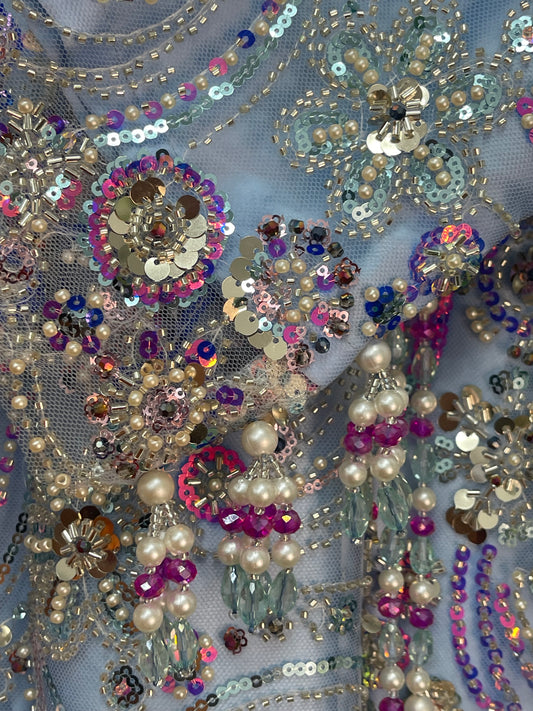 Close-up of decorative fabric with sequins, beads, and pearls on a gray background