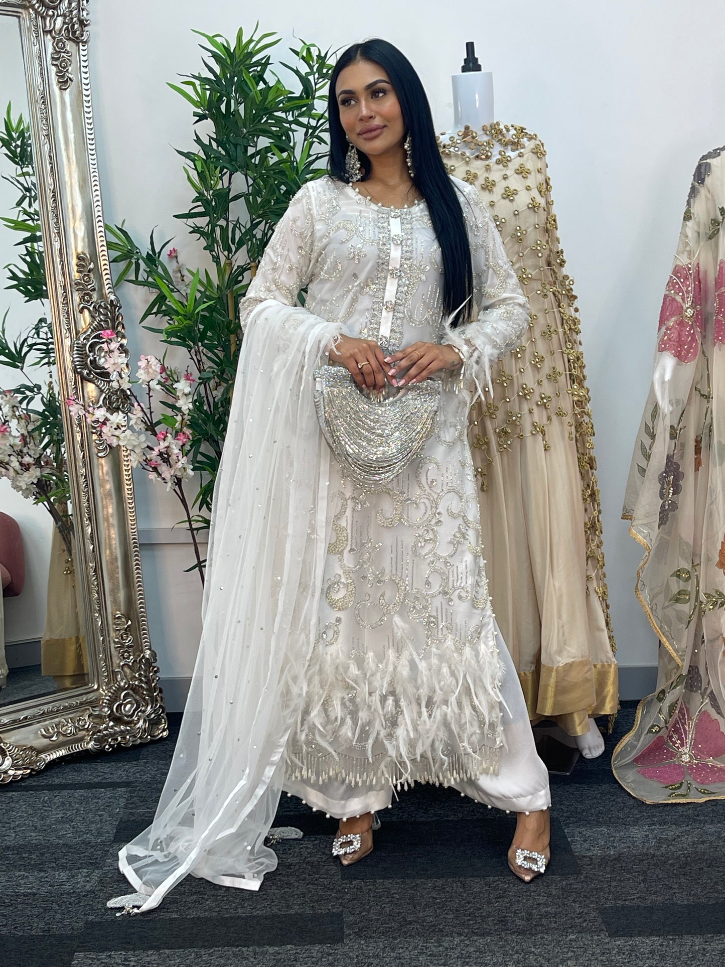 Woman in a white embroidered dress standing in front of a mirror with floral decorations.