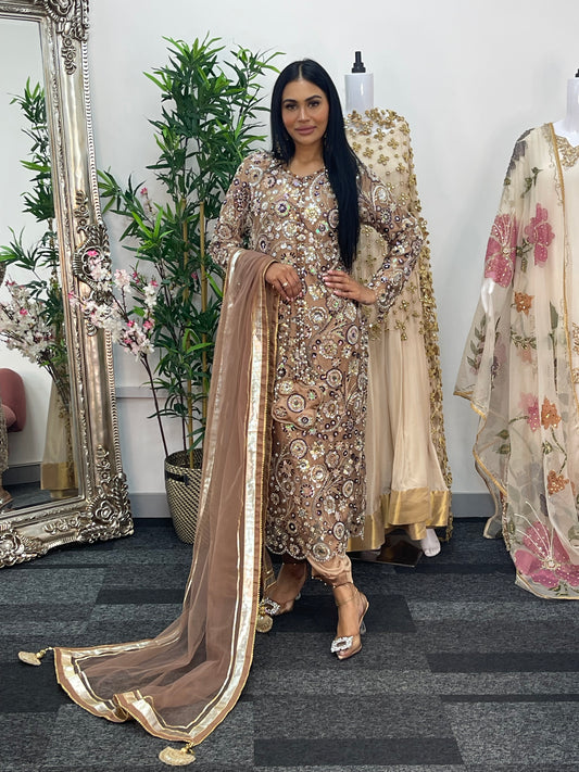 Woman in a traditional outfit standing next to a mannequin with a floral dress in a room.