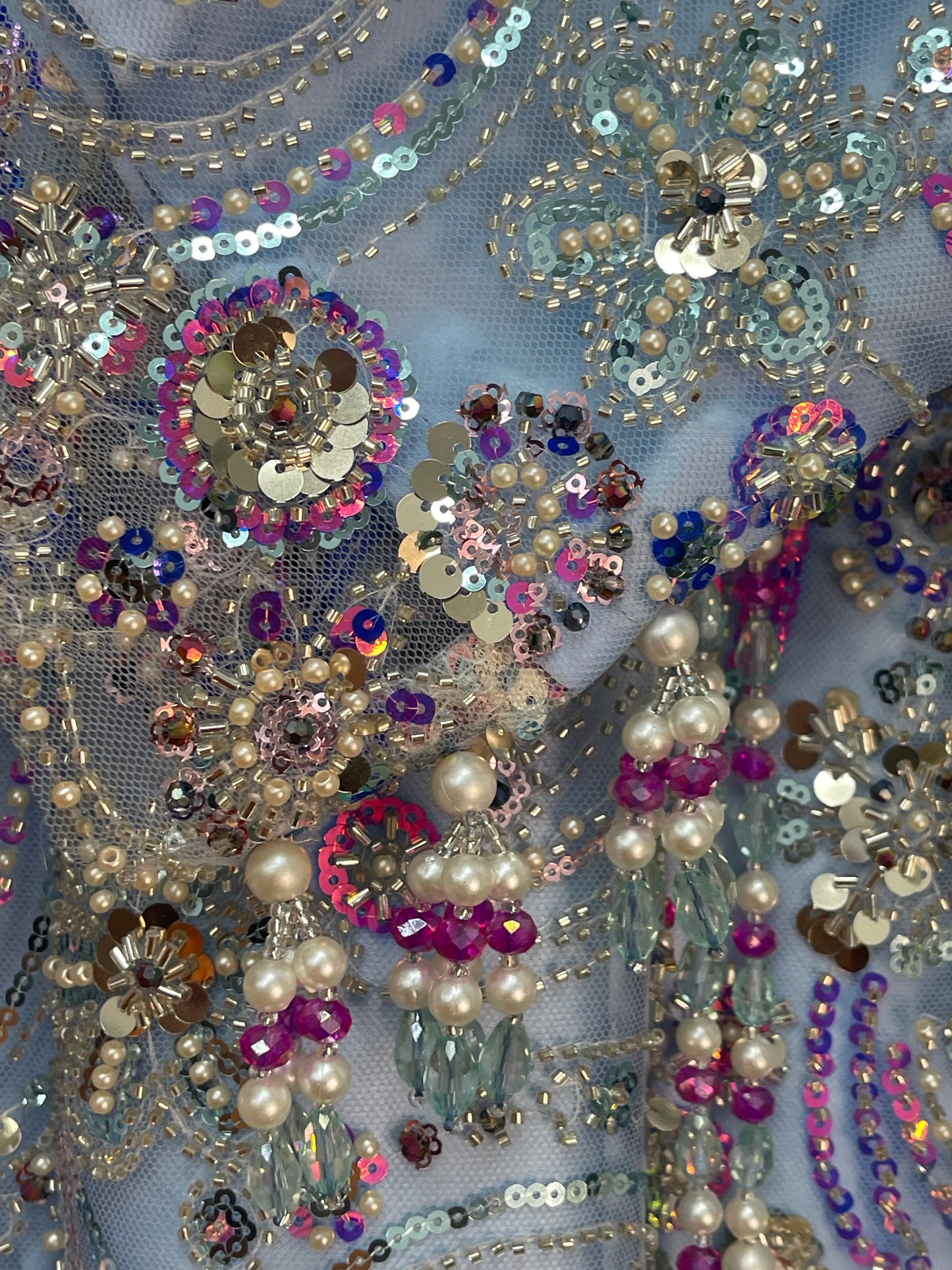 Close-up of decorative fabric with sequins, beads, and pearls on a gray background