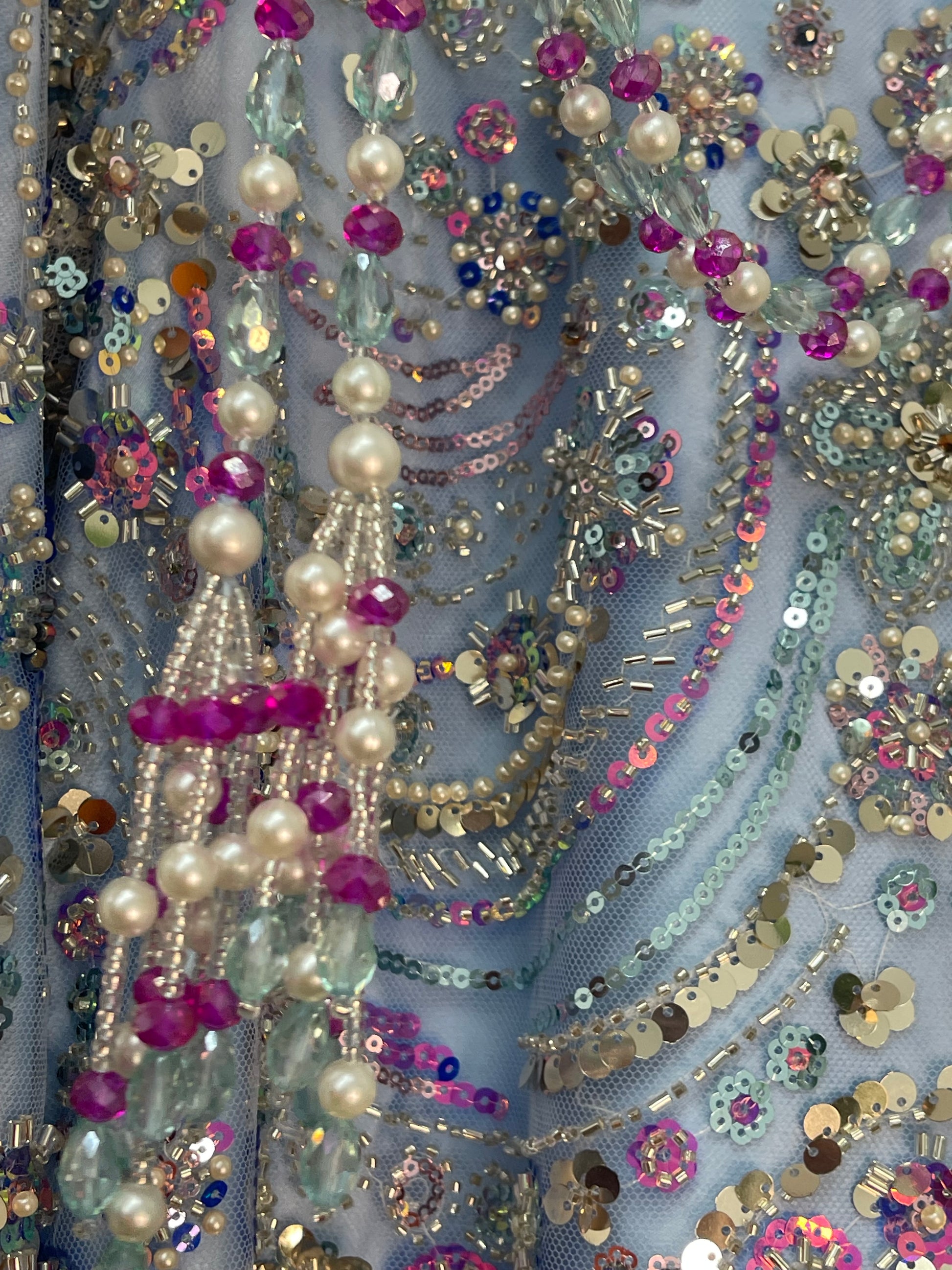Close-up of embellished fabric with pearls, sequins, and beads on a blue background