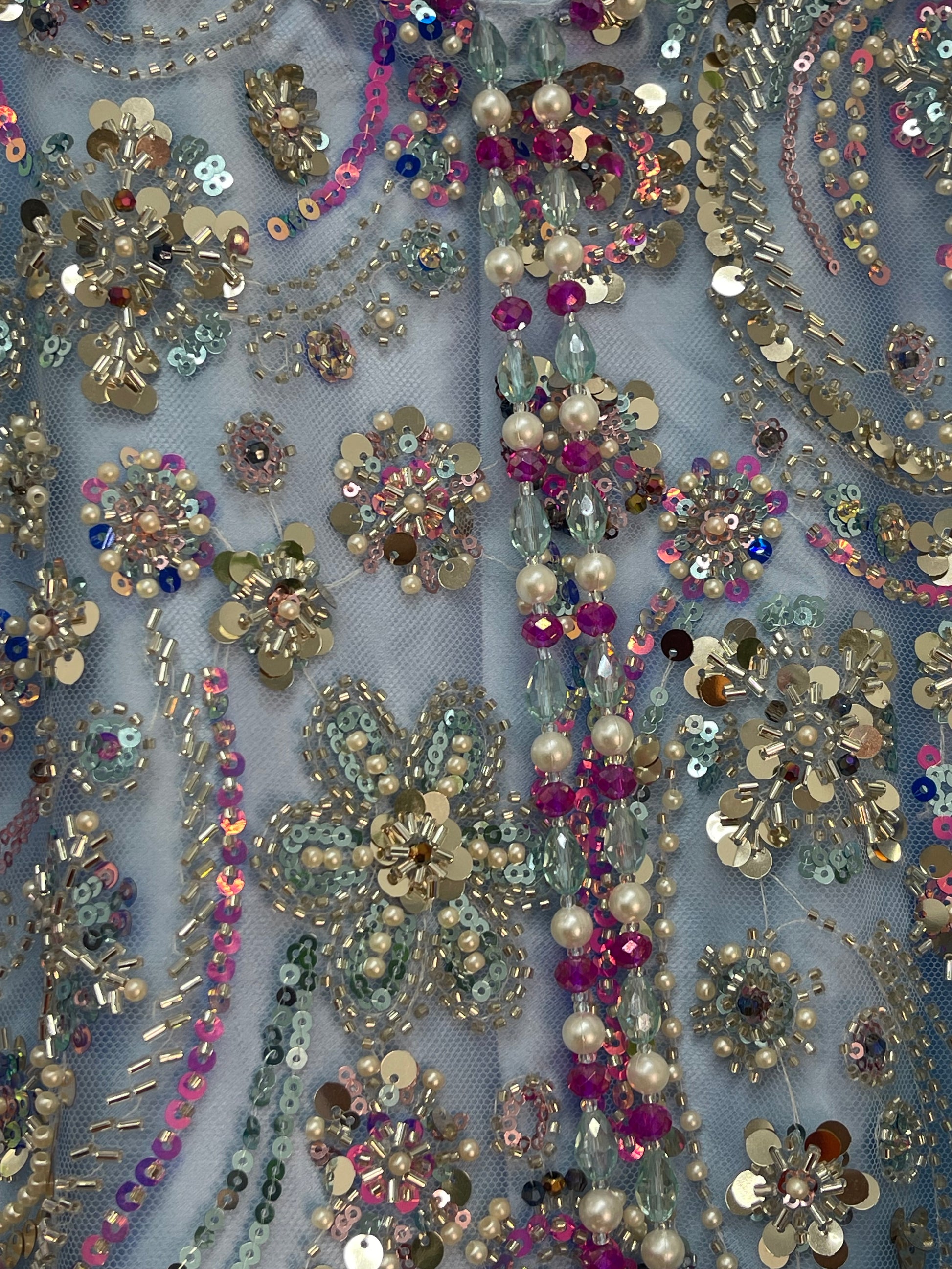 Close-up of decorative fabric with sequins, beads, and flowers on a light blue background