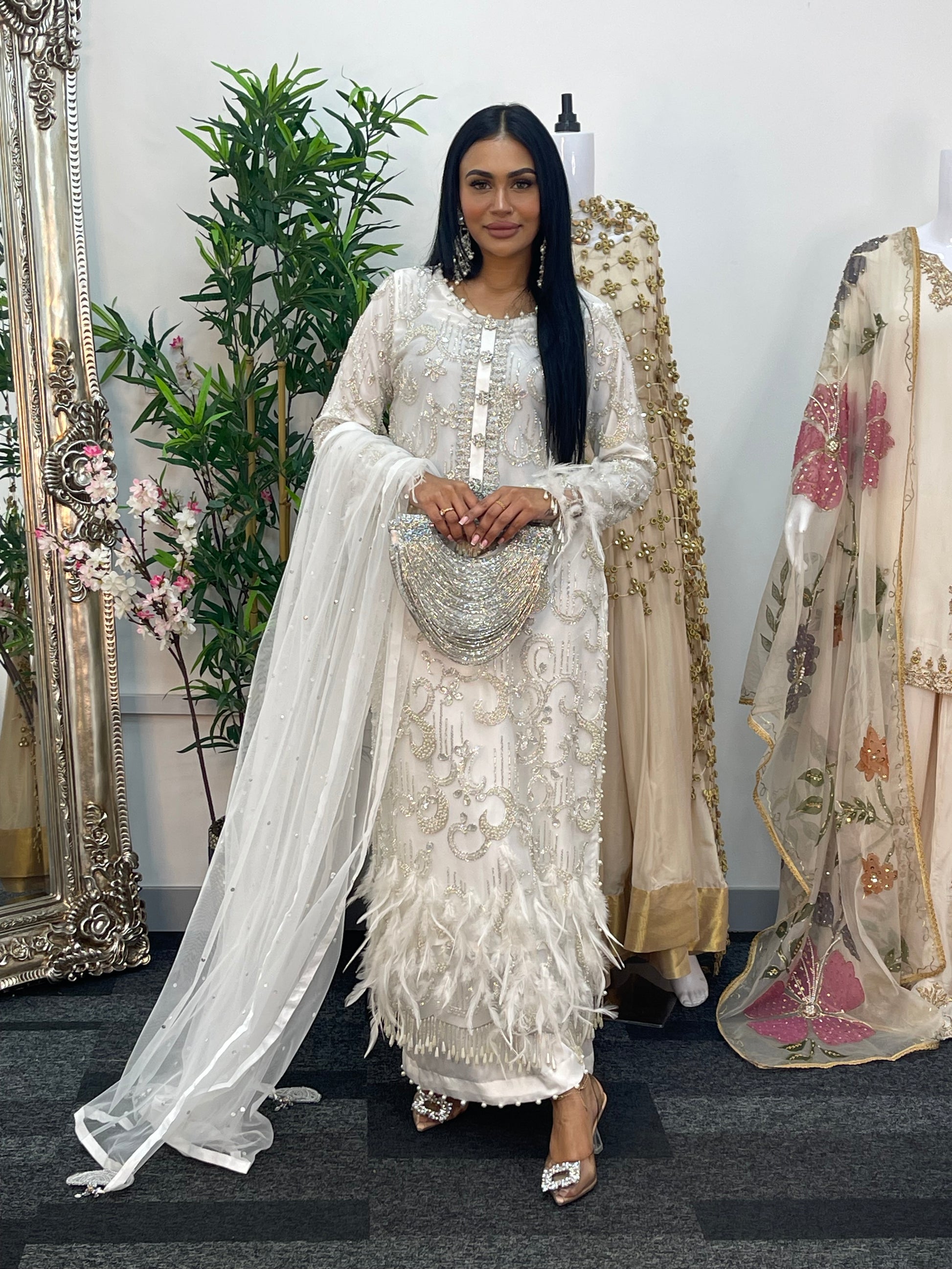 Woman in an embroidered traditional outfit standing in front of a mirror with floral decorations.