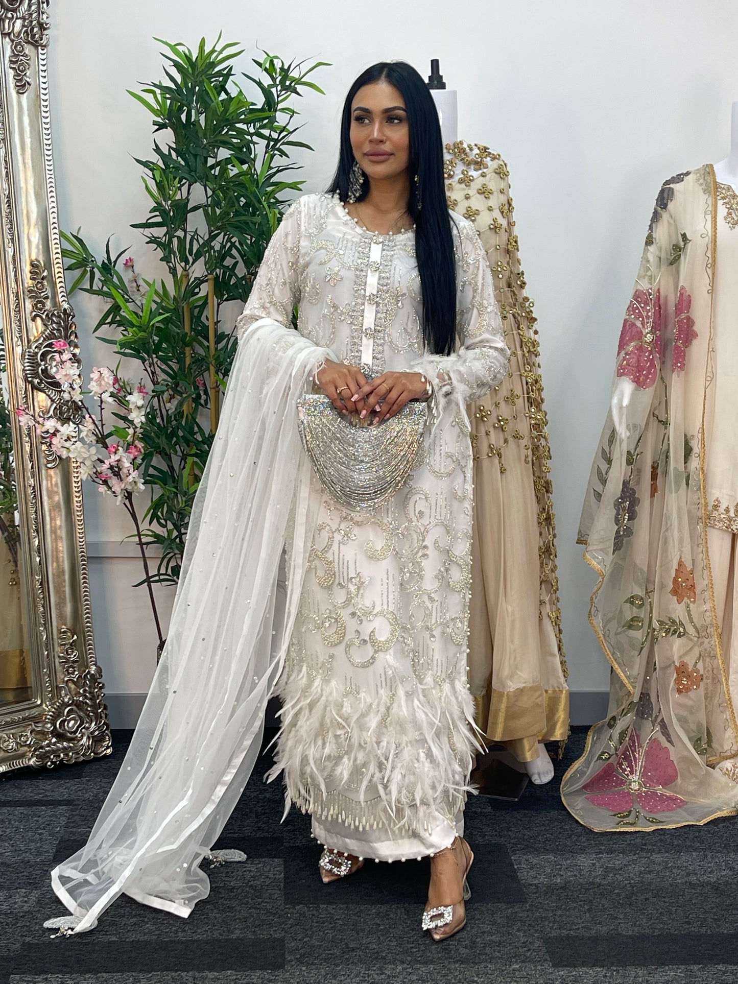 Woman in an ornate white dress standing in front of a mirror with floral decorations.
