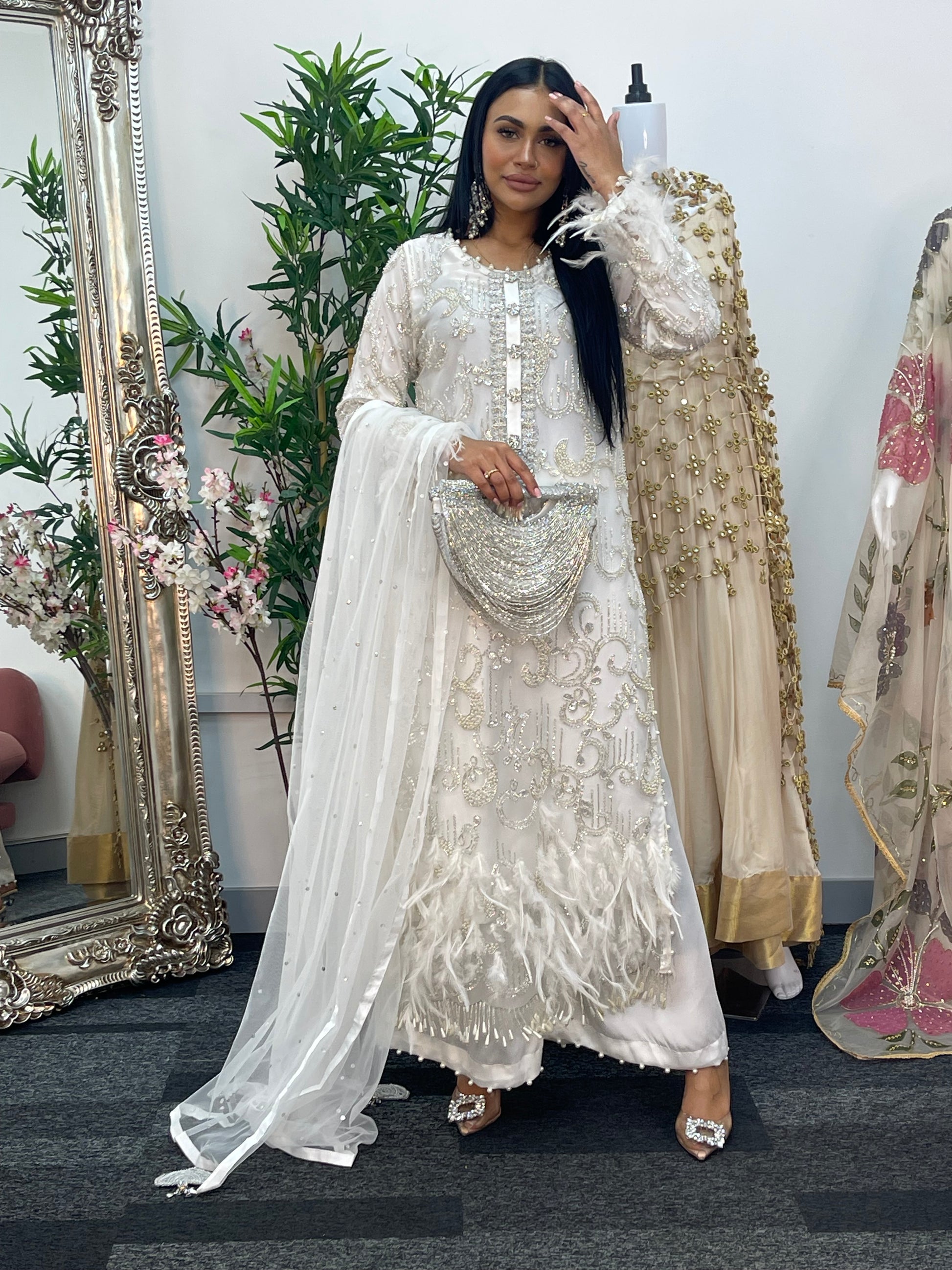 Woman in an embroidered traditional outfit standing in front of a mirror with floral decorations.