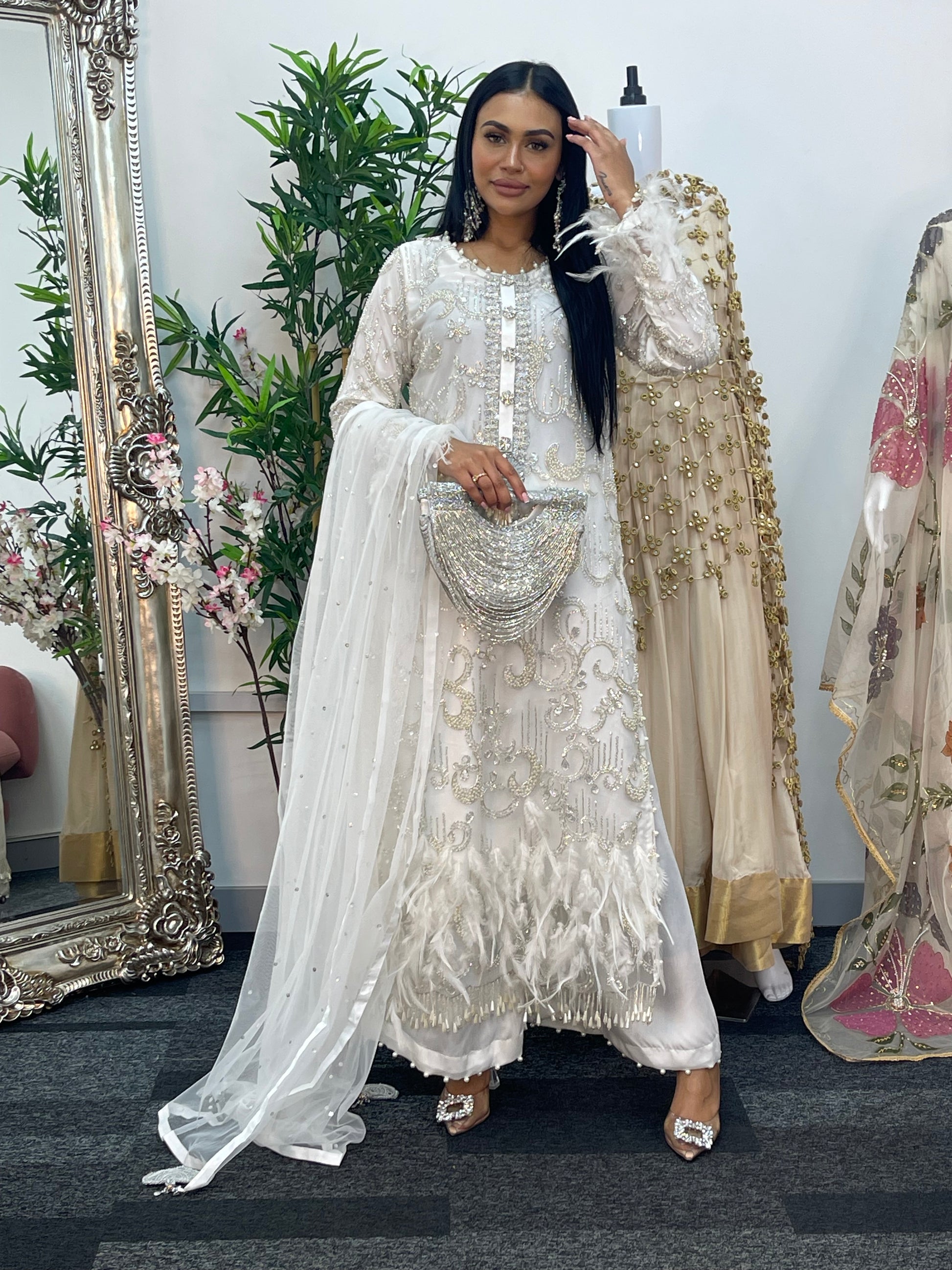 Woman in a white embroidered dress standing in front of a mirror with floral decorations.