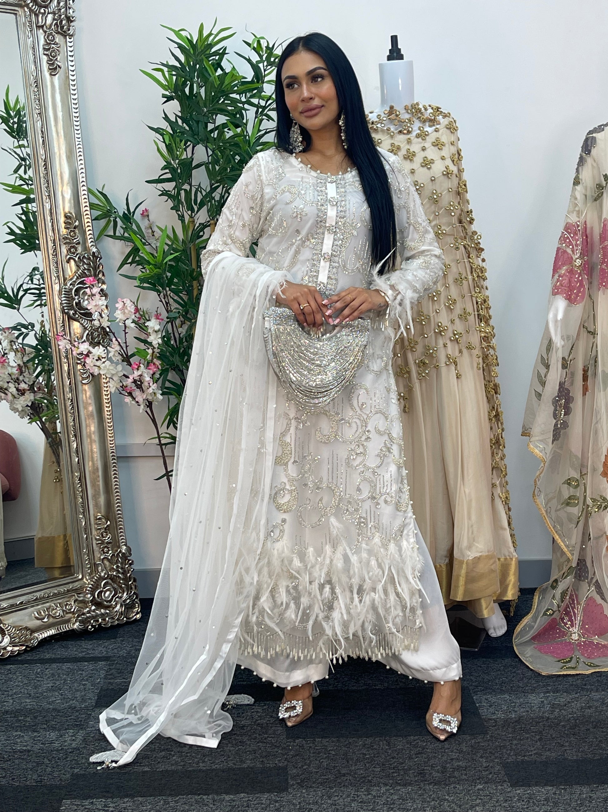 Woman in a white embroidered dress standing in front of a mirror with floral decorations.